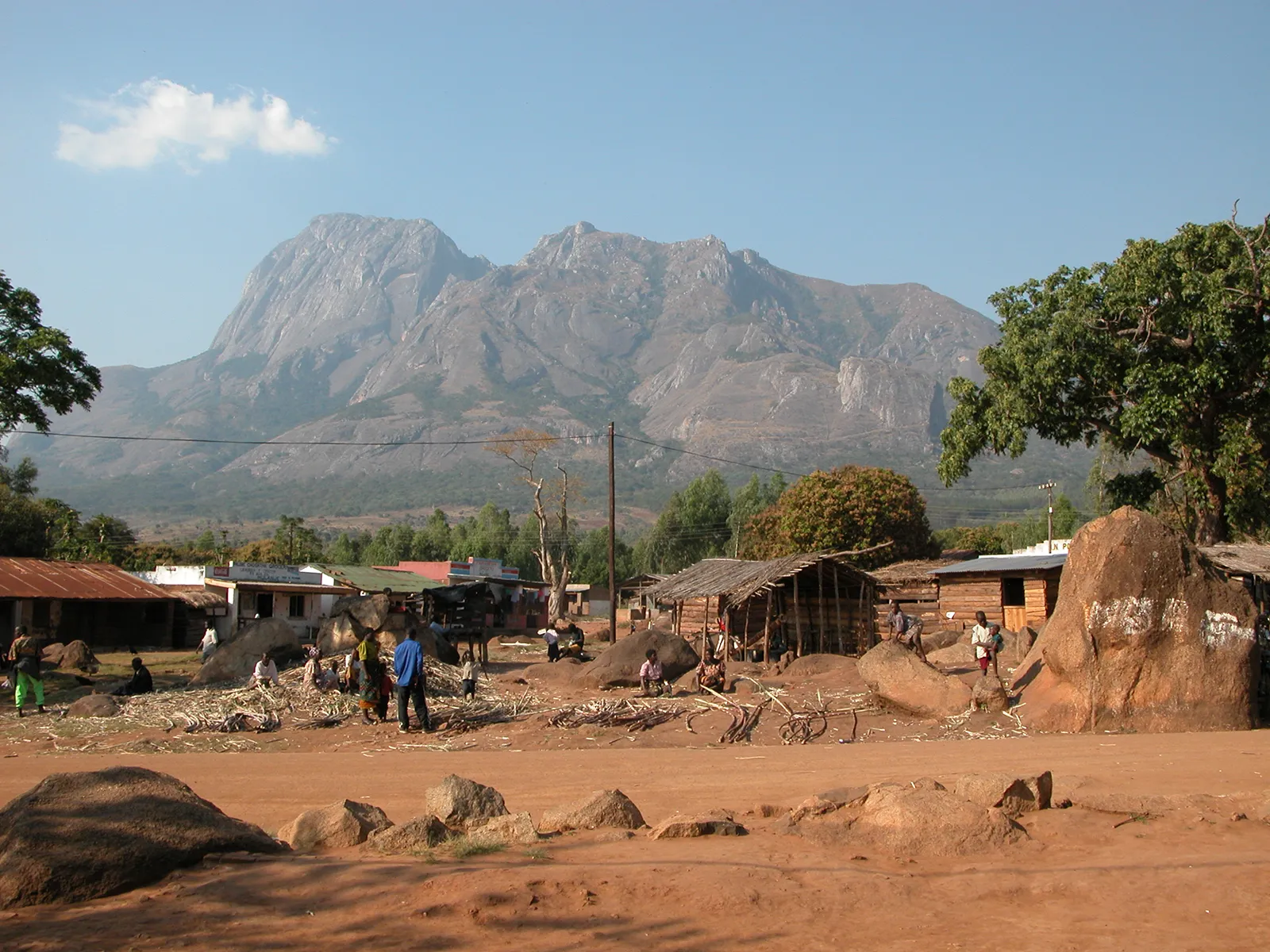 Malawi shacks built on red soil, with mountains in the background 